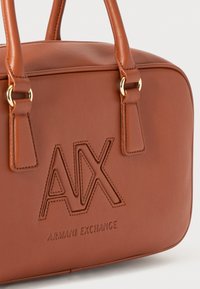 Brun läderhandväska med en strukturerad form, prydd med guldhandtag, präglad logotyp ("AX") och texturerade sömnadsdetaljer.