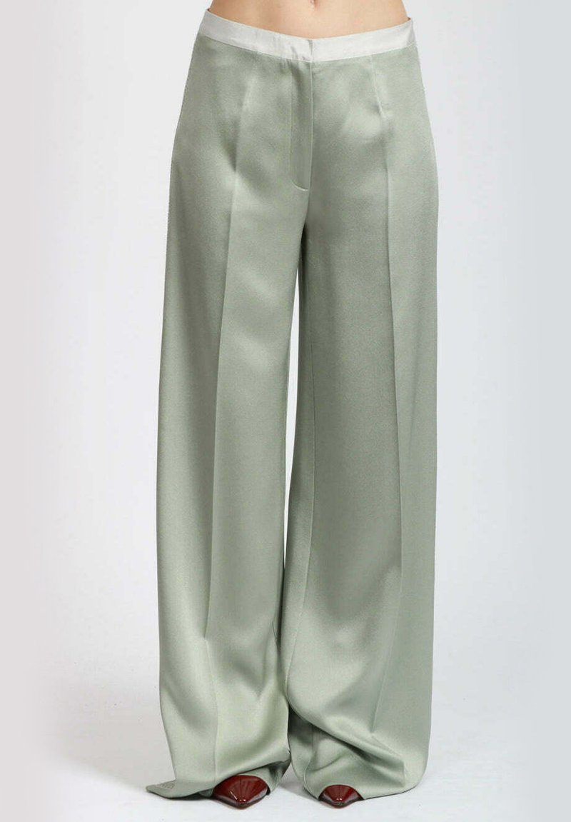 Pantaloni larghi di colore verde pallido, realizzati in un tessuto lucido e morbido con una cintura bianca a contrasto. Presentano pieghe frontali e una silhouette fluida.