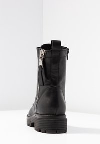 Botte de cheville en cuir noir avec une fermeture éclair latérale, une semelle texturée crantée et une languette de talon bouclée pour un enfilage facile. Finition lisse avec des détails de couture.