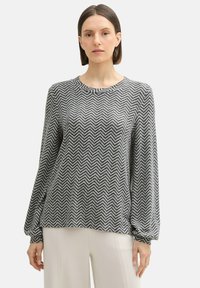 Suéter de manga larga con un patrón de espiga en blanco y negro, con cuello redondo y mangas ligeramente abullonadas, combinado con una parte inferior de color claro.