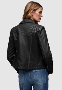Giubbotto in pelle nera con accenti trapuntati sulle spalle e un design aderente. La vista dal retro mostra una lunghezza leggermente accorciata e una texture liscia.