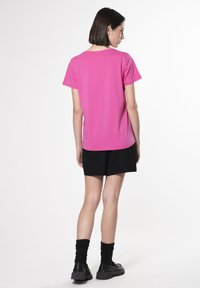 Camiseta de algodón rosa con cuello redondo, mangas cortas y corte relajado, combinada con pantalones cortos negros y calzado negro.