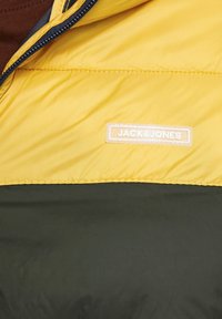 Padded jacket featuring a yellow upper with green lower section, zip closure, and a white label with "JACK&JONES." Smooth fabric texture.