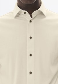 Krémszínű ing, textúrált felülettel, gombos záródással és sötét gombokkal az elején. Klasszikus gallérforma.