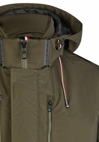 Olijfgroene geïsoleerde jas met hoge kraag, dubbele ritsen en verstelbare trekkoorden. Voorzien van een zwarte binnenvoering en gestructureerde stof.