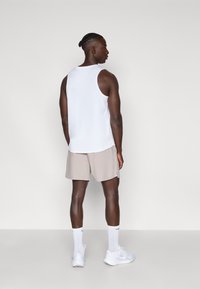 Λευκό αμάνικο μπλουζάκι σε συνδυασμό με ανοιχτό μπεζ σορτς, λευκά αθλητικά παπούτσια και λευκές κάλτσες. Απλός σχεδιασμός, κατάλληλος για αθλητικές δραστηριότητες.