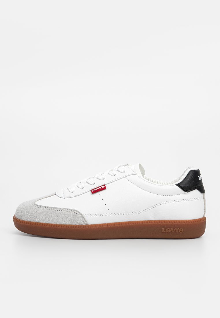 Zapatilla blanca con puntera de ante gris, acento negro en el talón y suela de goma marrón. Presenta un diseño de cordones y un logotipo rojo en el lateral.