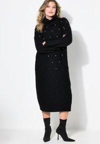 Schwarzes Rollkragen-Strickkleid mit gerippten Bündchen und Saum. Präsentiert ein Diamantmuster und perlartige Akzente zur Detailverfeinerung. Kombiniert mit schwarzen Absatzstiefeln.