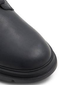 Zapato de cuero azul marino con punta redondeada, superficie texturizada y suela de goma con ranuras horizontales para mayor agarre.