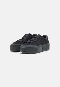 Sneakers negre din suede, cu o talpă din cauciuc texturat, groasă, având șireturi plate și un design cu vârf rotund. Branding minimal pe limbă.