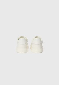 Baskets blanches avec tige en cuir lisse, col rembourré et semelle en caoutchouc texturé. Présente un design minimaliste sans marque visible.