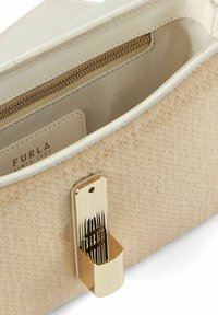 Borsa in pelle beige con texture e interno liscio e chiaro. Presenta una chiusura dorata e dettagli con tasca con zip. L'etichetta riporta la scritta "FURLA SINCE 1927."