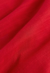 Tessuto di lino rosso con una texture liscia, che mostra sottili variazioni di tonalità e intreccio, creando un aspetto morbido e fluido.