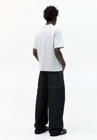 Grå kortærmet polo shirt med lige kant, parret med løstsiddende mørk denim jeans med baglommer og hvid syning.