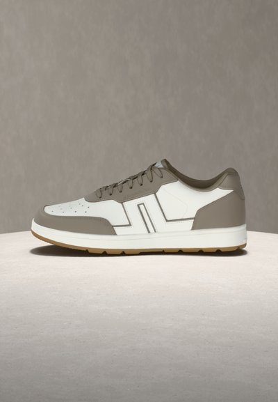 Χαμηλό αθλητικό παπούτσι με λευκά και ταουπέ πάνελ, διάτρητη μύτη, κλείσιμο με κορδόνια και λαστιχένια σόλα πάνω σε φωτεινή επιφάνεια με υφή.