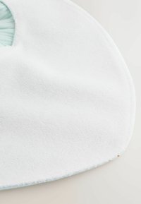 Pehmeä, valkoinen, pyöreä vauvan ruokalappu, jossa on teksturoitu kangas ja pieni mintunvihreä joustava kaula-aukko.