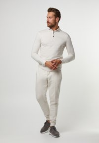 Light beige long-sleeve polo with three buttons, paired with matching jogger pants. Soft texture, casual fit, and elastic waistband. Gray sneakers.