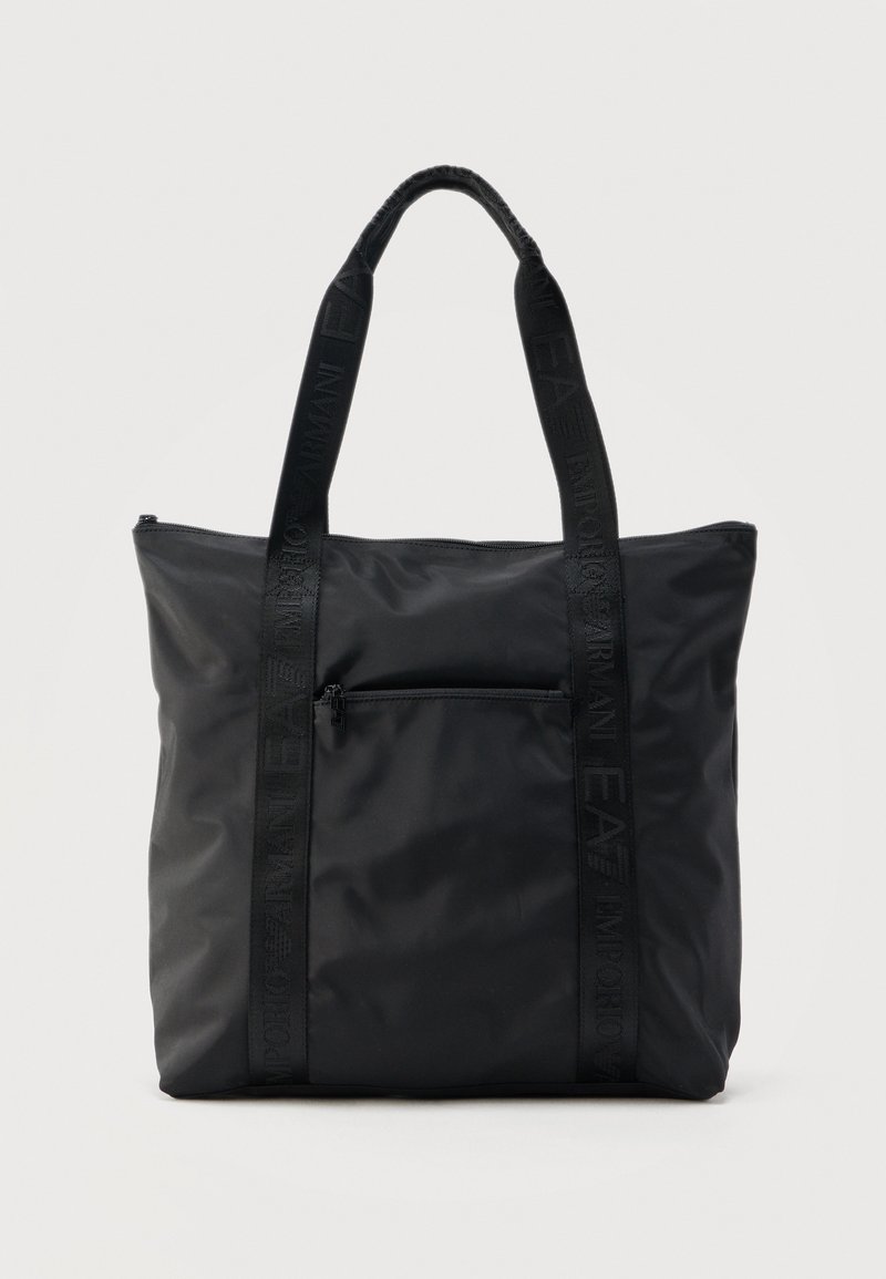 Sac fourre-tout en nylon noir avec deux longues bandoulières et une poche zippée à l'avant, fond uni.