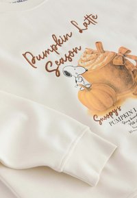 White sweatshirt with illustration of Snoopy, pumpkins, a whipped cream-topped latte, and text reading "Pumpkin Latte Season."