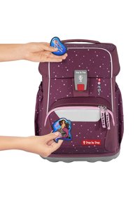 Lila Rucksack mit Sternmuster, ausgestattet mit einer Fronttasche und zwei dekorativen Aufnähern. Verfügt über einen grauen Griff und Reißverschlussakzenten.