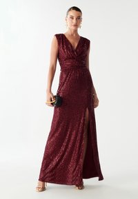 Burgundi vahtidegaga õhtukleit sügava V-kaelusega, ilma varrukateta, vöökoht detailidega ja kõrge reiesilma lõikega. Kanna musta kotiga.