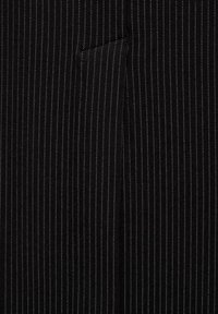 Tessuto nero con sottili strisce bianche verticali. La texture sembra liscia e c'è un dettaglio della tasca visibile sul lato sinistro.
