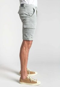 Lichtgrijze cargoshorts met zijzakken, omgeslagen zoom en een relaxte pasvorm, gecombineerd met beige sneakers met witte veters.