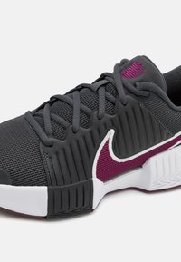 Grå atletiksko med netoverdel og vertikale kanter, hvide accenter og en burgunderrød Nike swoosh. Holdbar sål med teksturerede mønstre.