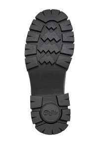 Suela de goma negra con surcos profundos y una superficie texturizada. Presenta un logo redondeado en el talón. Diseñada para ofrecer tracción y durabilidad.