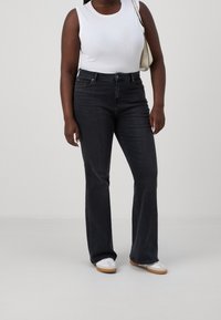 Jeans neri a zampa d'elefante con vita alta, dotati di tasche frontali e passanti per cintura, abbinati a una maglietta senza maniche bianca e sneakers bianche.