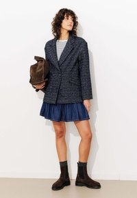 Blazer en velours bleu marine avec un devant croisé, haut rayé, jupe en denim et bottines en daim marron avec des côtés élastiques.