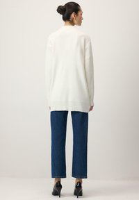 Valge suurte mõõtmetega kampsun koos soonikkoega varrukate ja äärega, kombineeritud tumesiniste sirgete teksade ja mustade kõrgete kontsadega jalanõudega.