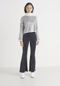Striped black and white knit sweater with a high neckline paired with flared black pants featuring a subtle pattern and white heeled boots.