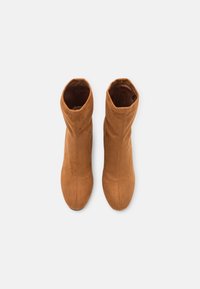 Bottines en daim couleur fauve avec une forme effilée, une texture lisse et des détails cousus. Les bordures sont légèrement retroussées en haut pour le design.