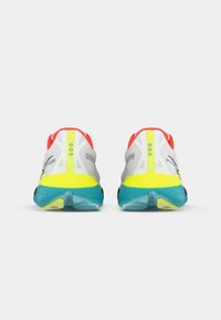 Zapatillas de correr con una parte superior de malla gris, acentos rojos y un talón amarillo brillante. Presentan una suela turquesa y detalles en negro.