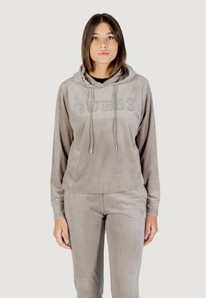 Haut de survêtement en velours gris clair avec "GUESS" en strass, doté d'une poche kangourou à l'avant et d'une capuche avec cordon de serrage. Accompagné d'un pantalon assorti.