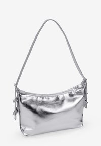 Bolso de hombro metálico plateado con una textura suave, cierre con cremallera y acentos decorativos de hardware en los laterales. Forma cilíndrica con una sola correa.