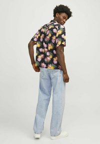 Camisa de manga corta con fondo negro, con patrones florales coloridos en rosa, amarillo y verde; combinada con jeans de un azul claro.