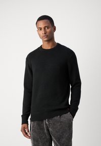 Suéter negro de punto con escote redondo, puños acanalados y dobladillo. Combinado con pantalones rayados grises, que muestran una tela texturizada.