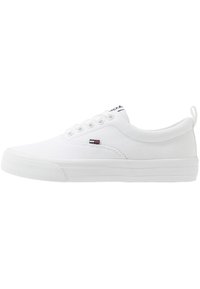 Vit tygsneaker med gummisula, snörning och sydda detaljer. Har en liten logotyp på sidan och en mjuk inredning.