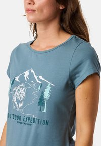 Light blue short-sleeve t-shirt made of soft fabric, featuring a graphic design of a bear, mountains, and trees with text "Outdoor Expedition."