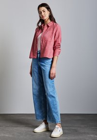 Vaaleanpunainen pitkähiha, jossa on rintataskut, yhdistettynä löysiin vaaleansinisiin farkkuihin ja valkoisiin tennareihin. Yksinkertainen, rento istuvuus.