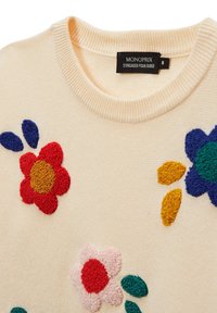 Pull en tricot crème clair avec broderies florales colorées rouges, bleues, jaunes et vertes. Il présente un col rond côtelé.
