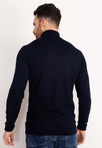 Donkerblauwe sweater met een hoge kraag, slanke pasvorm en geribbelde boorden. De textuur lijkt zacht en dicht gebreid, met een eenvoudig ontwerp.