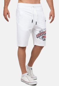 Witte katoenen shorts met een elastische tailleband, zijzakken en contrasterende zwarte trekkoorden. Voorzien van een logo-opdruk in rood en zwart.