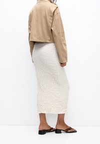 Veste courte beige, jupe midi blanche texturée et sandales à enfiler à imprimé animal. Tissu lisse et silhouette structurée.