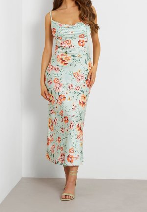 Kvinde iført en ærmeløs, lyseblå midi-kjole med orange og pink blomsterprint og tynde stropper, kombineret med lysegrønne ankelremssandaler.