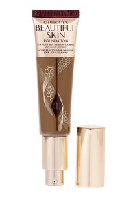 Charlotte's Beautiful Skin Foundation tube with gold pump dispenser and cap, in medium-dark shade with decorative lines and chemical motifs.