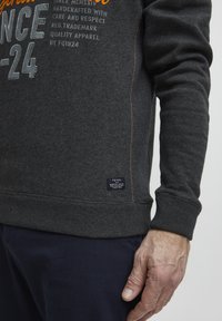 Dark grey sweatshirt with orange and white text. Features ribbed cuffs, a tag at the hem, contrast stitching, and a relaxed fit.