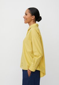 Camicia gialla a maniche lunghe con bottoni, orlo curvo, fessure laterali e vestibilità rilassata, realizzata in tessuto leggero.